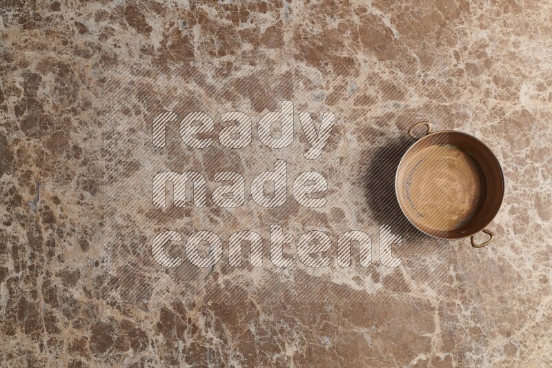 A small copper pan on beige marble background