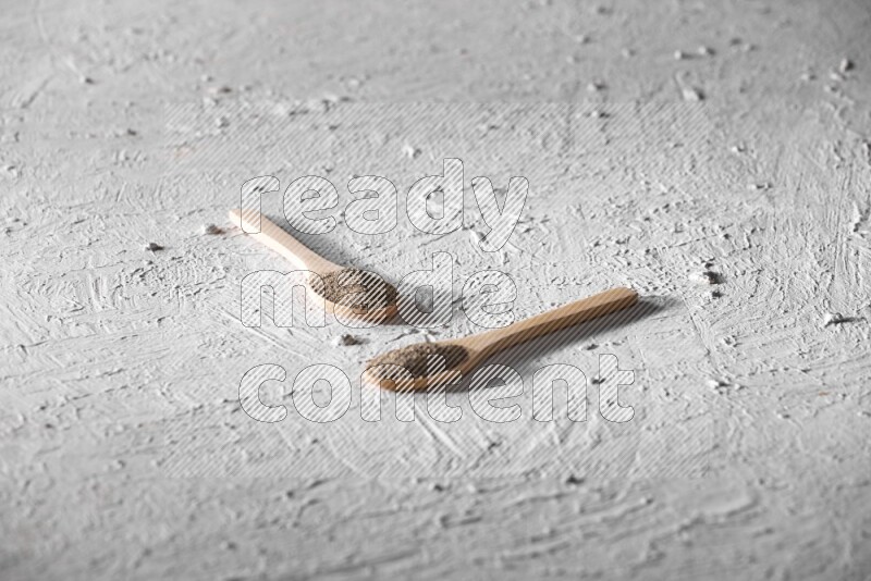 2 wooden spoons full of black pepper powder on a textured white background