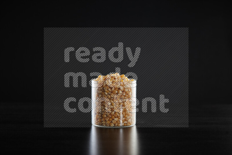 Dry corn kernels in a glass jar on black background