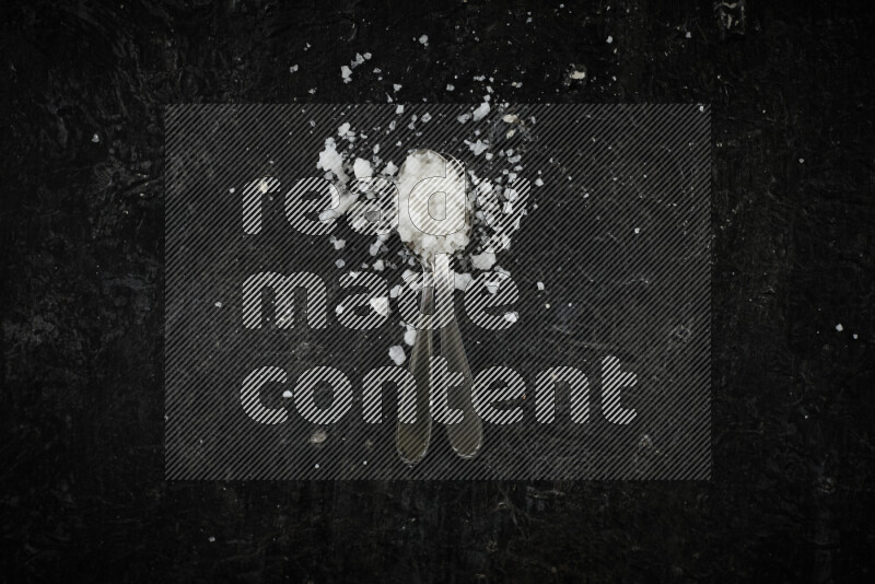 2 metal spoons filled with white salt on black background