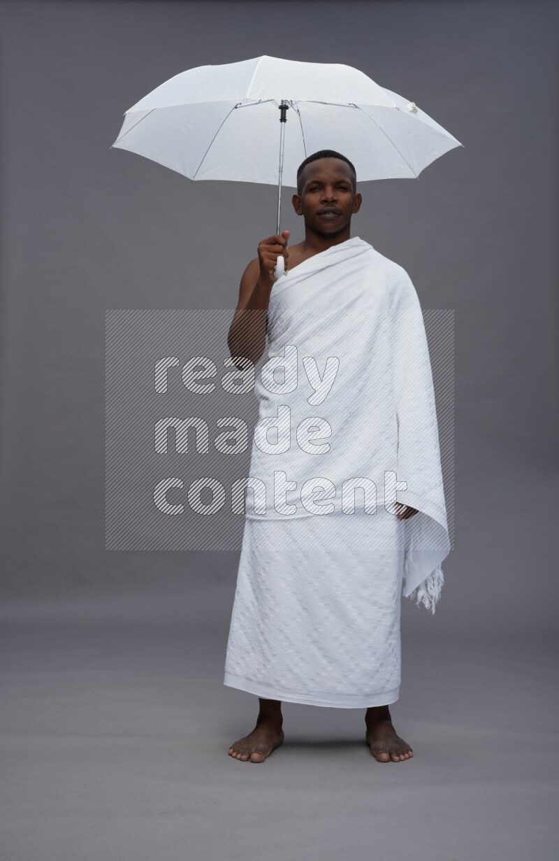 A man wearing Ehram Standing holding umbrella on gray background