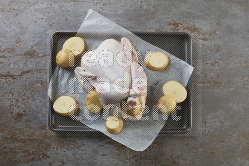 whole raw chicken on an oven trey direct on a rustic grey background