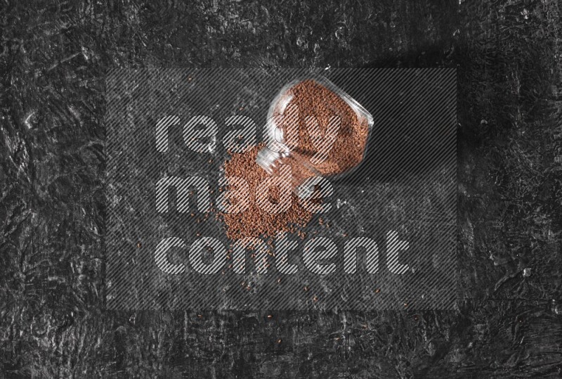 A glass spice jar full of garden cress seeds flipped and seeds spread out a textured black flooring