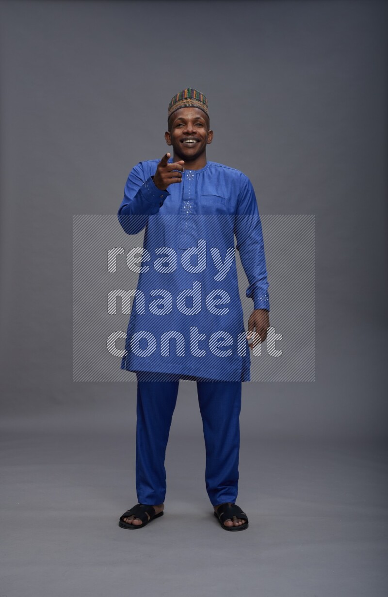 Man wearing Nigerian outfit standing interacting with the camera on gray background
