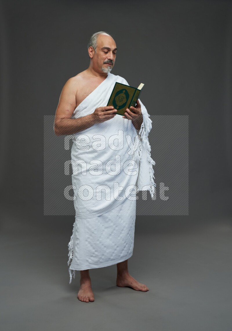 A man wearing Ehram Standing reading quran on gray background