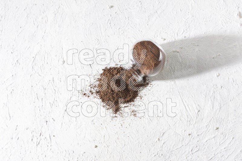 A flipped glass spice jar full of cloves powder and powder came out of it on textured white flooring