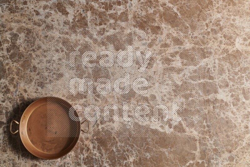 A small copper pan on beige marble background