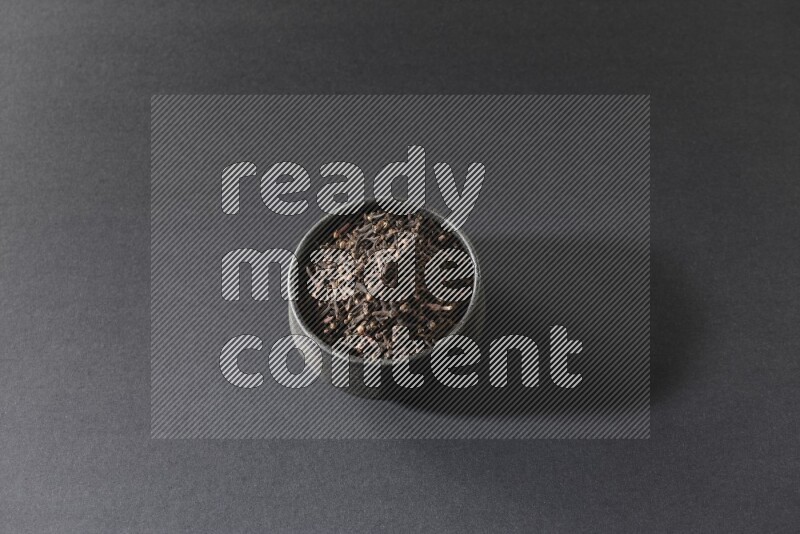 A black pottery bowl full of cloves on a black flooring