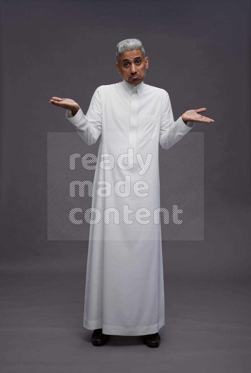 Saudi man wearing thob standing interacting with the camera on gray background