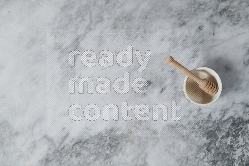 وعاء فخاري بيج مع ملعقة عسل خشبية بداخله على خلفية من الرخام الرمادي