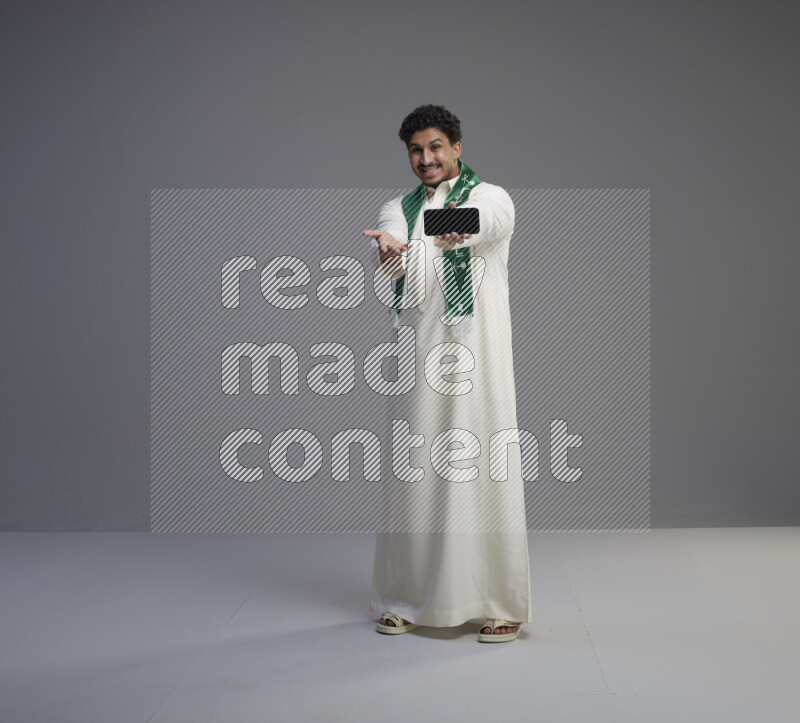 رجل سعودي يرتدي ثوب ابيض و شال يحمل جوال