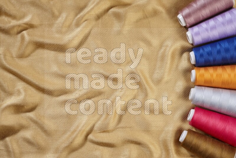 Multicolored sewing thread spools on yellow fabric background