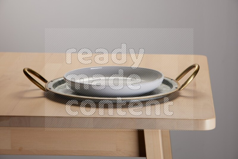 white plate placed on a rounded stainless steel tray with golden handels on the edge of wooden table