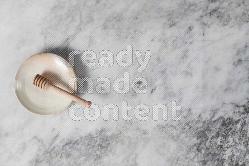 Beige pottery plate with wooden honey dipper in it on grey marble background