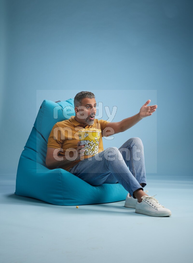 A man sitting on a blue beanbag and eating popcorn