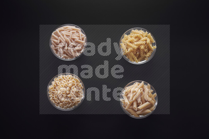 Different pasta types in glass bowls on black background