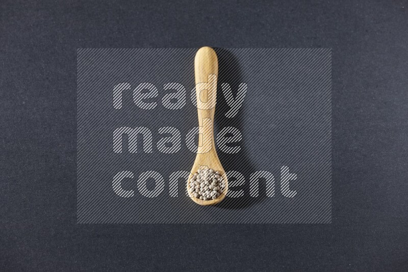 A wooden spoon full of white pepper beads on black flooring