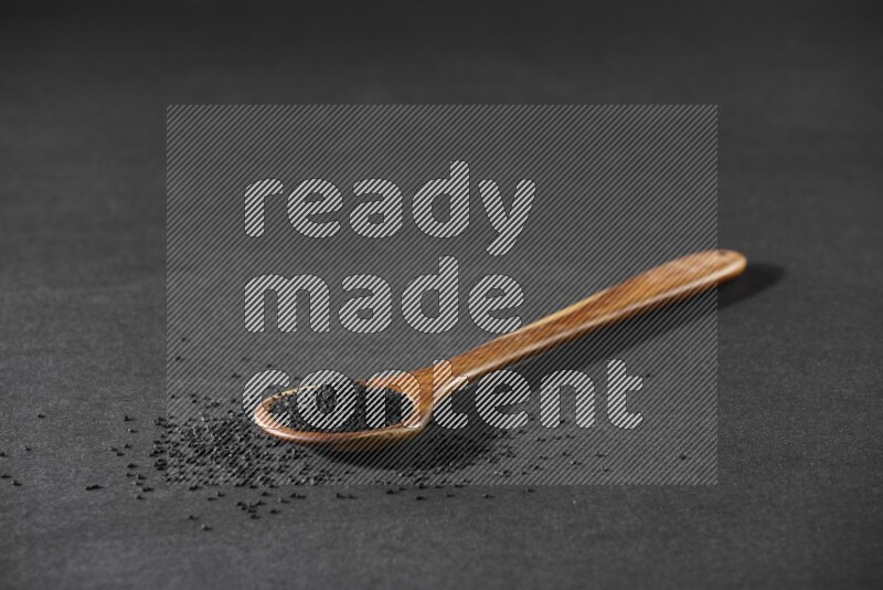 A wooden ladle full of black seeds and the seeds spread beside it on a black flooring