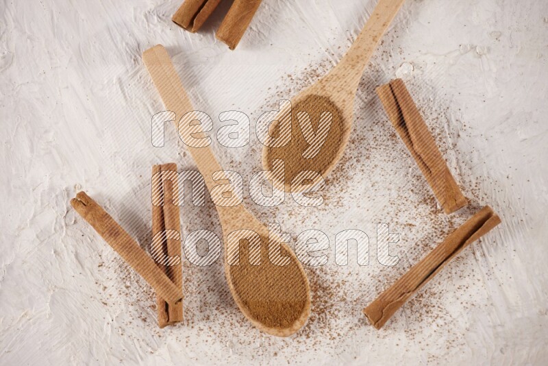 Two wooden spoons full of cinnamon powder with cinnamon sticks on white background