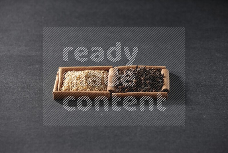 مربعان من أعواد القرفة ممتلئان ببذور السمسم والقرنفل علي خلفية سوداء