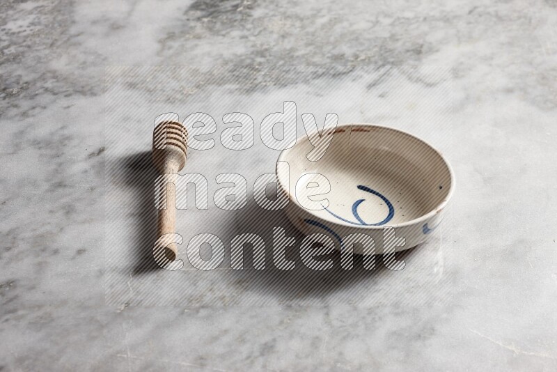 Multicolored pottery bowl with wooden honey dipper on the side on grey marble background