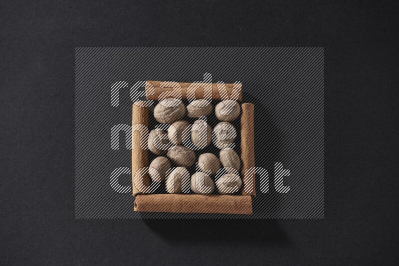 أربعة من أعواد القرفة مكونة شكل مربع بداخلها جوزة الطيب علي خلفية سوداء