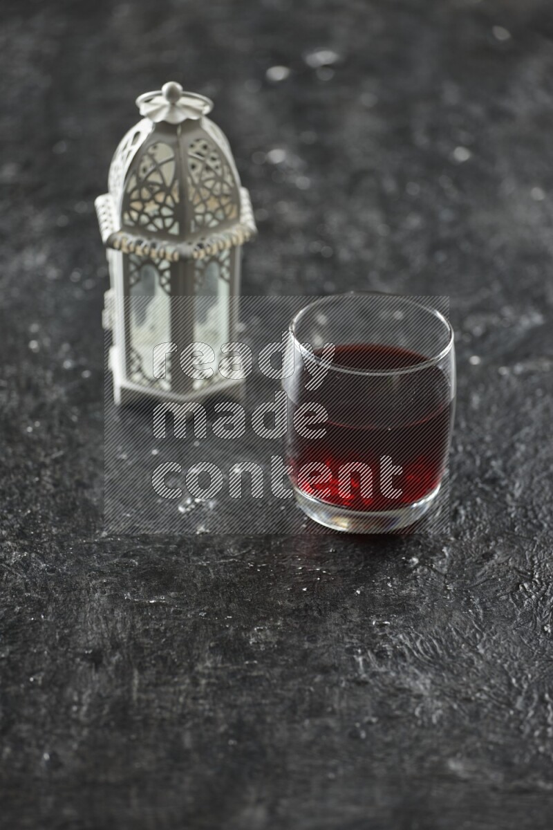 A white lantern with different drinks, dates, nuts, prayer beads and quran on textured black background