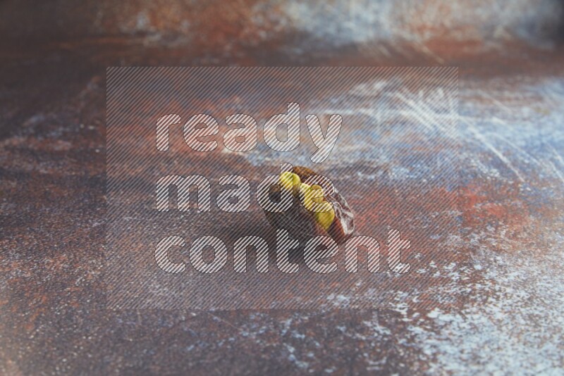 one pistachio stuffed madjoul date on a rustic reddish background
