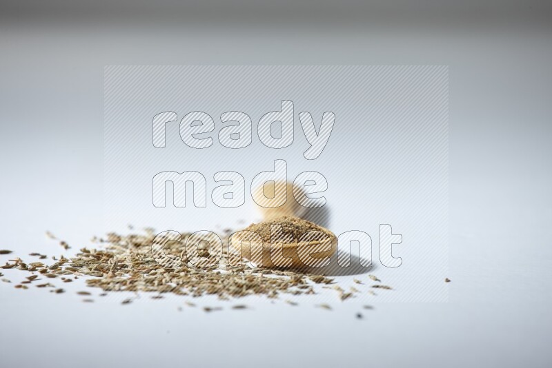 A wooden spoon full of cumin powder and cumin seeds beside it on white flooring