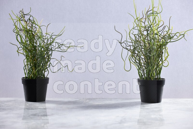 Two green artificial plants in black pots on grey marble background
