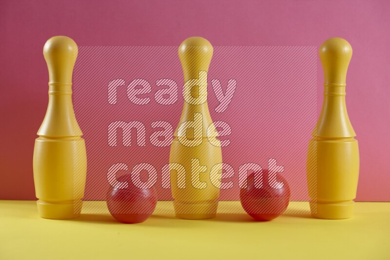 Plastic bowling pins with balls on pink and yellow background (kids toys)