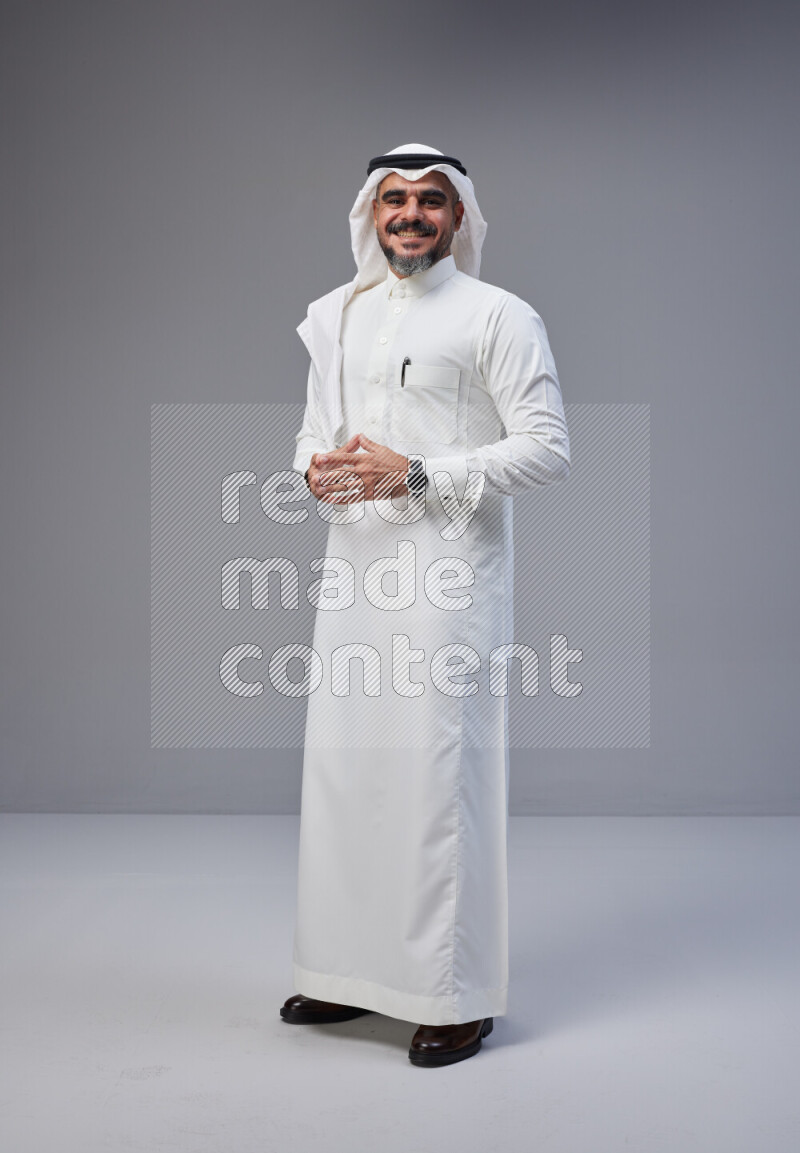 Saudi man Wearing Thob and white Shomag standing interacting with the camera on Gray background
