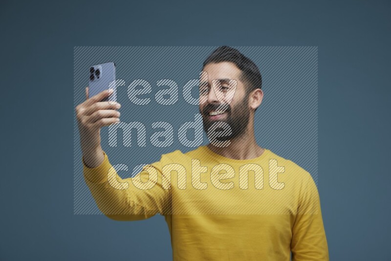 Man Taking a Selfie  in a blue background wearing a yellow shirt