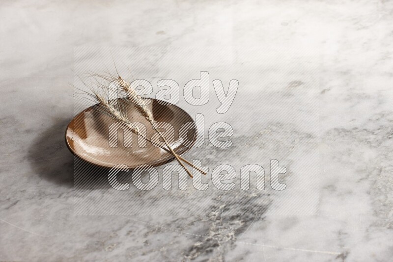 Wheat stalks on multicolored pottery plate on grey marble background