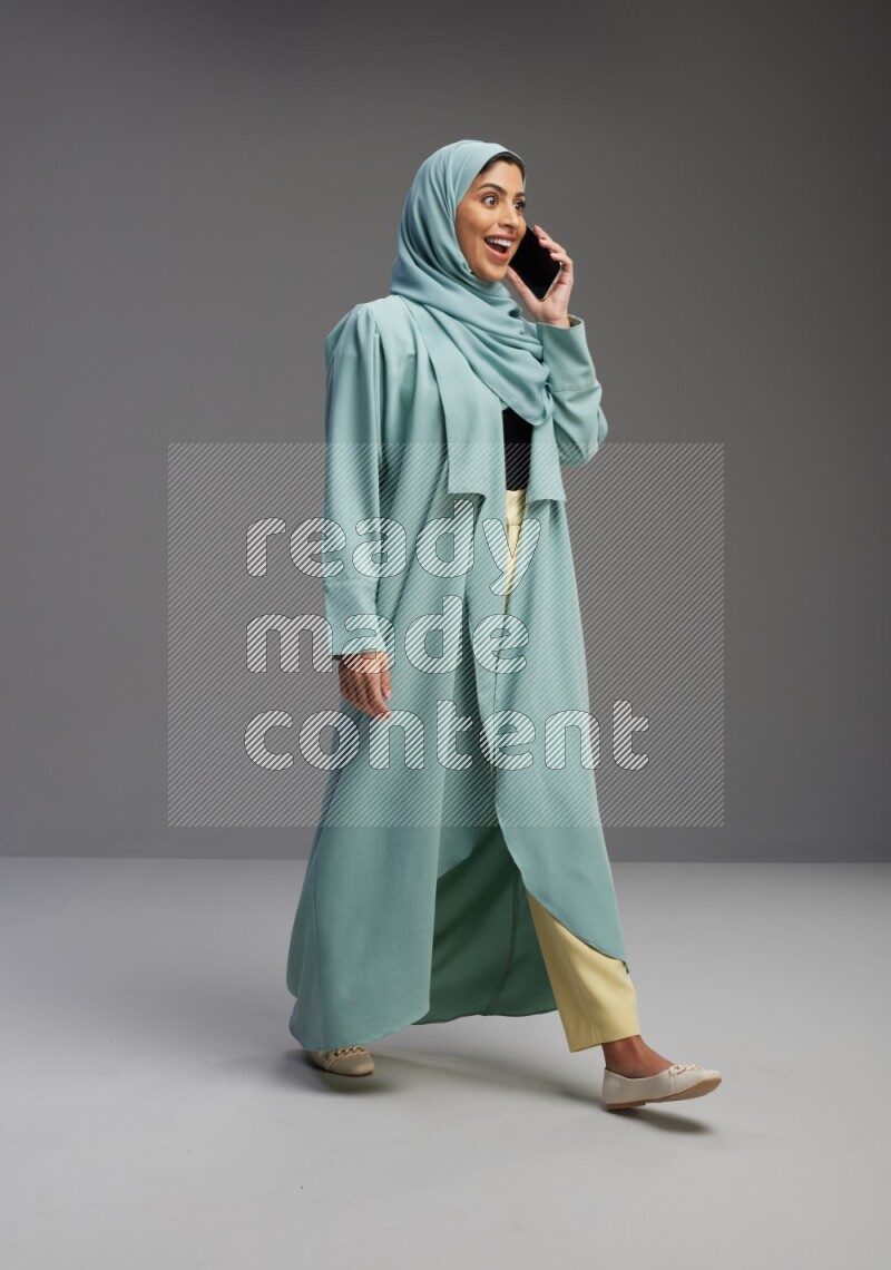 Saudi Woman wearing Abaya standing talking on phone on Gray background