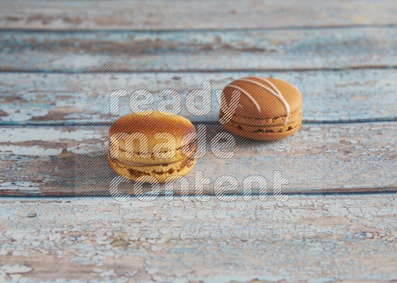 45º Shot of of two assorted Brown Irish Cream, and Yellow Crème Brulée macarons on light blue background