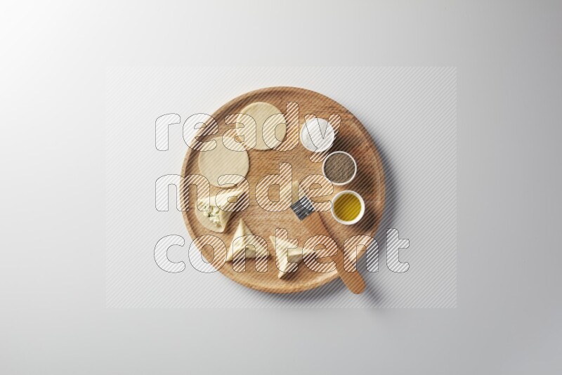 two closed sambosas and one open sambosa filled with cheese while salt, black pepper and oil with oil brush aside in a wooden dish on a white background