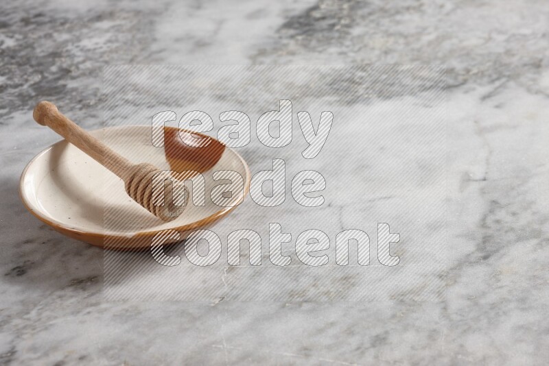Multicolored pottery plate with wooden honey dipper in it on grey marble background