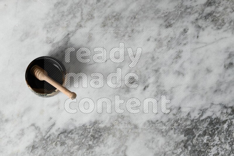 وعاء فخاري متعدد الألوان مع ملعقة عسل خشبية بداخله على خلفية من الرخام الرمادي