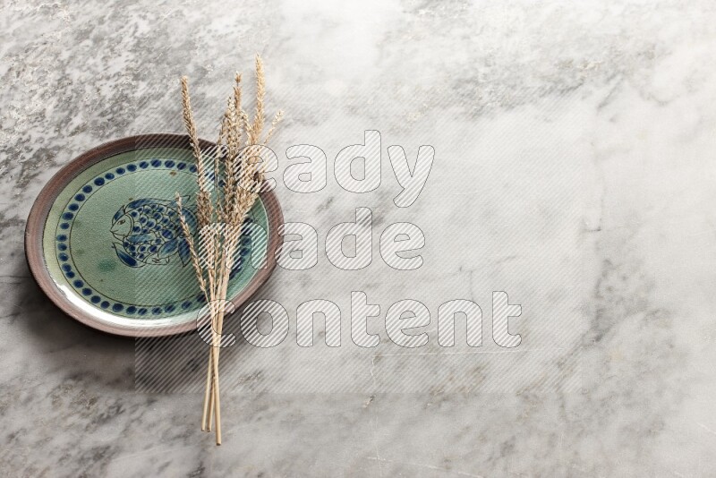 Wheat stalks on decorative pottery plate on grey marble background