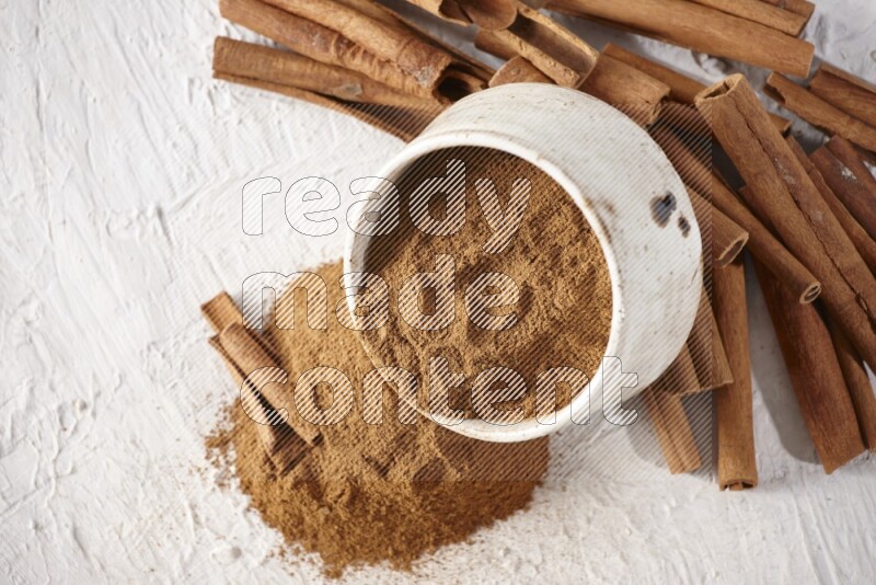 Ceramic beige bowl over filled with cinnamon powder and cinnamon sticks around the bowl on a textured white background in different angles