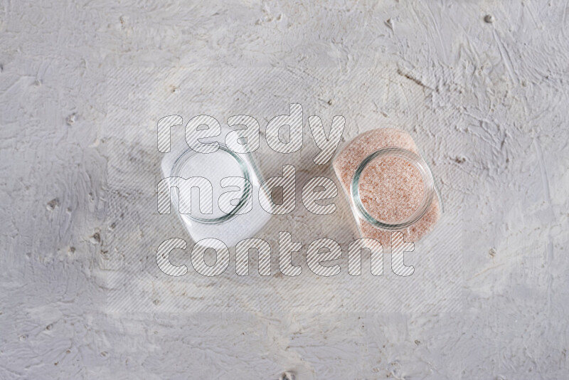 2 وعاء زجاجي احدهمها ممتلئ بملح الهيمالايا الناعم والأخر بملح الطعام على خلفية بيضاء