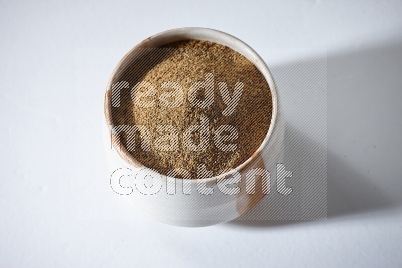 وعاء بيج ممتلئ ببودرة الكمون على خلفية بيضاء