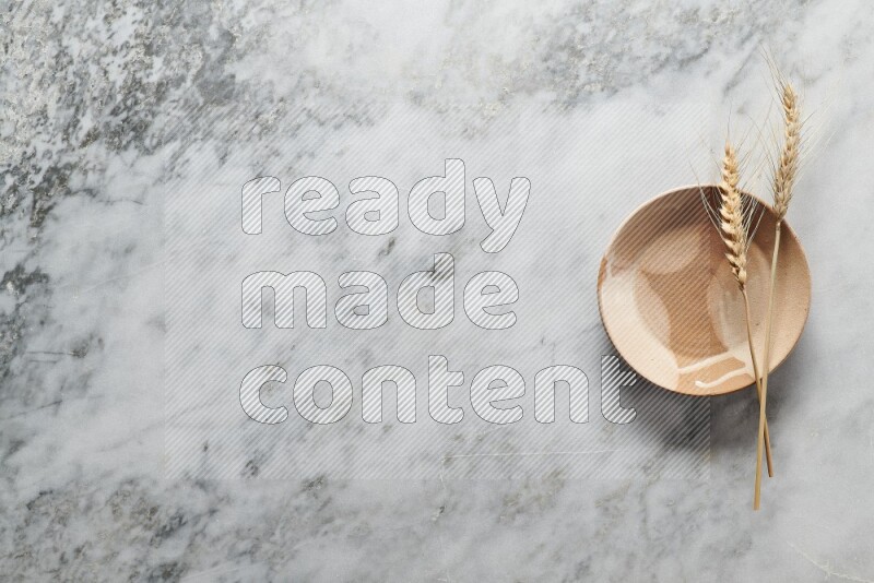 Wheat stalks on multicolored pottery plate on grey marble background