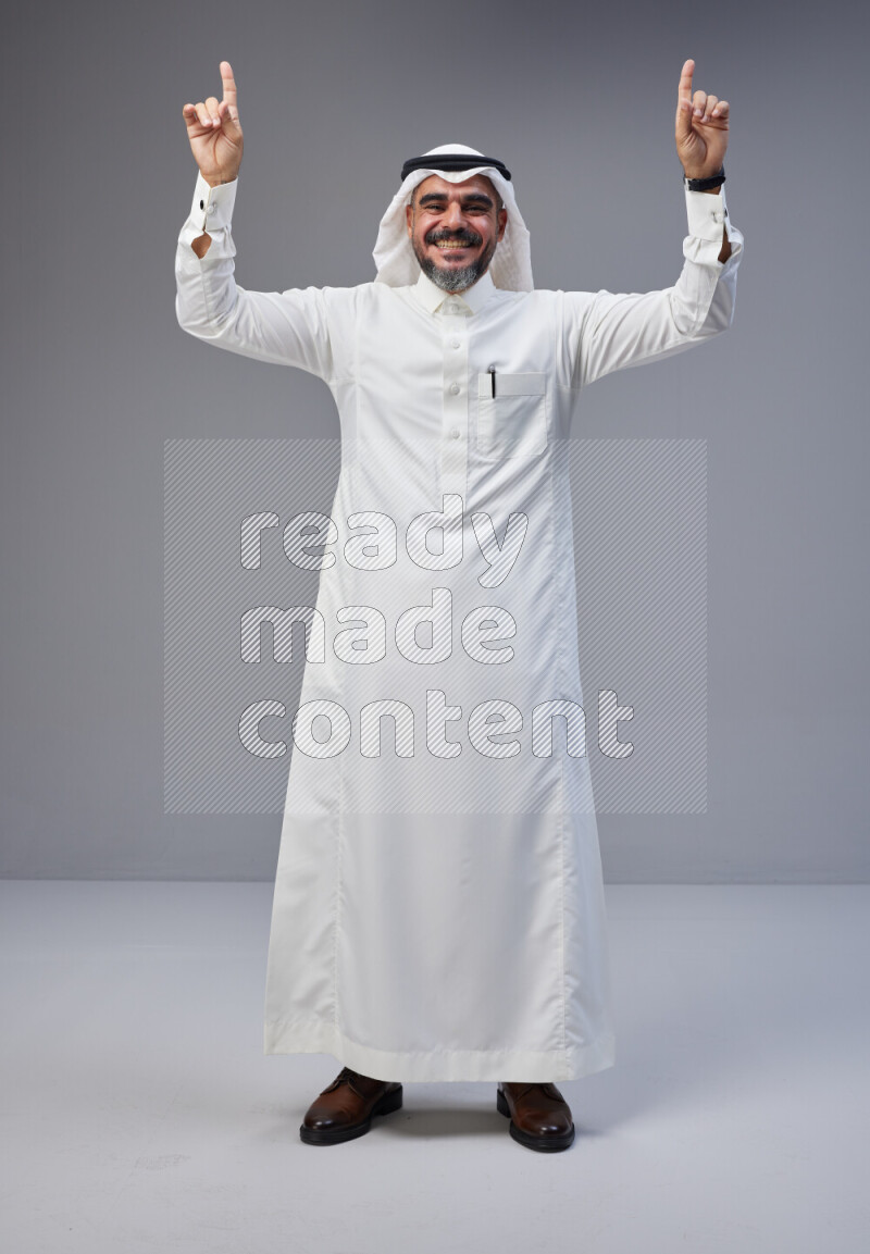 Saudi man Wearing Thob and white Shomag standing interacting with the camera on Gray background