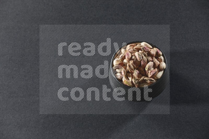 A black pottery bowl full of peeled pistachios on a black background in different angles