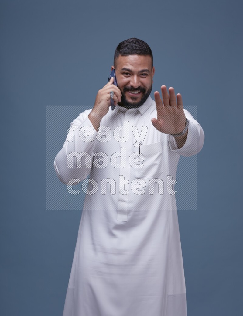 A Saudi man calling on blue background wearing Saudi Thob