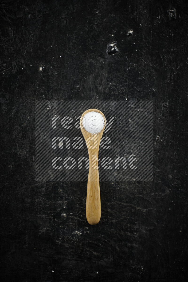 A wooden spoon full of white salt on black background