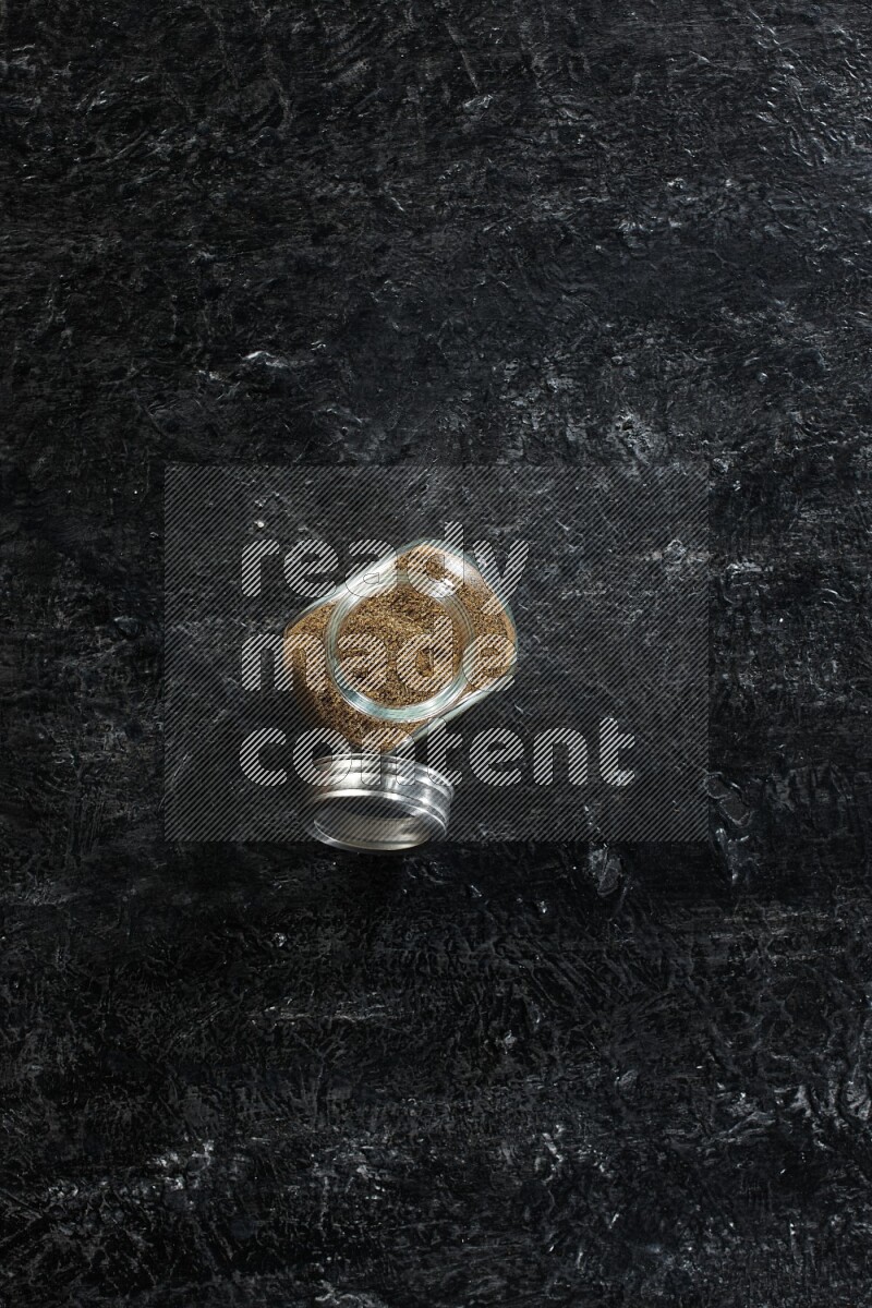 وعاء زجاجي للتوابل ممتلئ ببودرة الكمون على خلفية سوداء