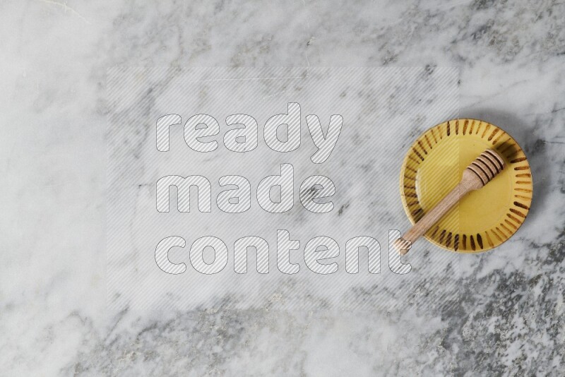 طبق فخاري متعدد الألوان مع ملعقة عسل خشبية بداخله على خلفية من الرخام الرمادي